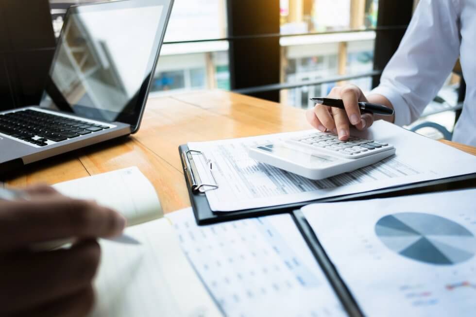 Close-up of people working on financial documents with a calculator, laptop, and charts at a desk.